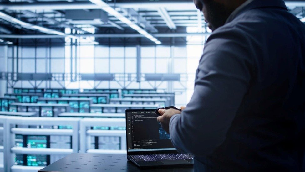 A tech professional operates a laptop in a data center filled with server racks.